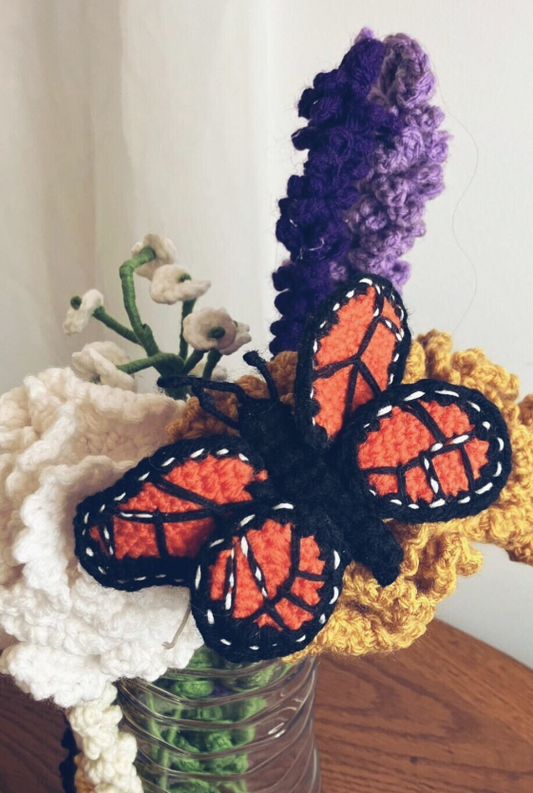 Crocheted Monarch butterfly handmade with orange, black, and white yarn, resting on a neutral surface. Perfect for home or office décor, or as a unique handmade gift.